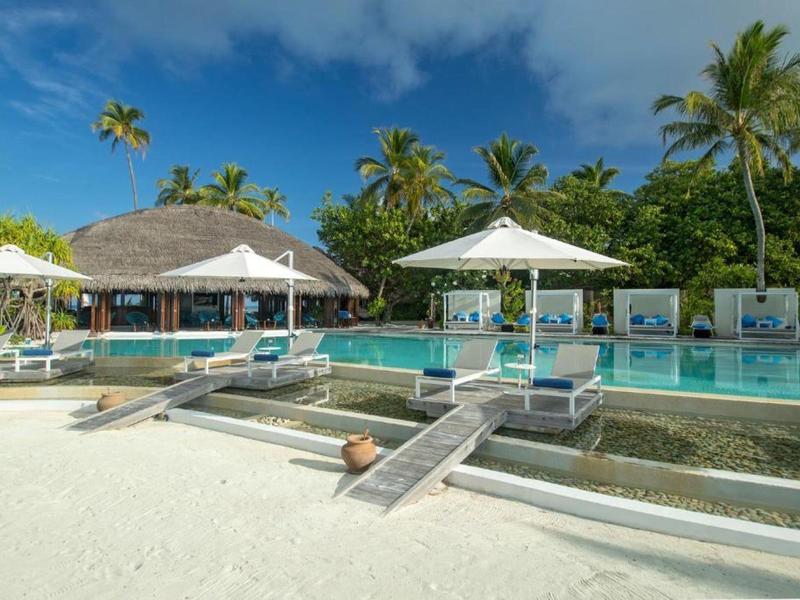 Resort di lusso sulla spiaggia con piscina, ombrelloni e vegetazione tropicale sotto un cielo azzurro.