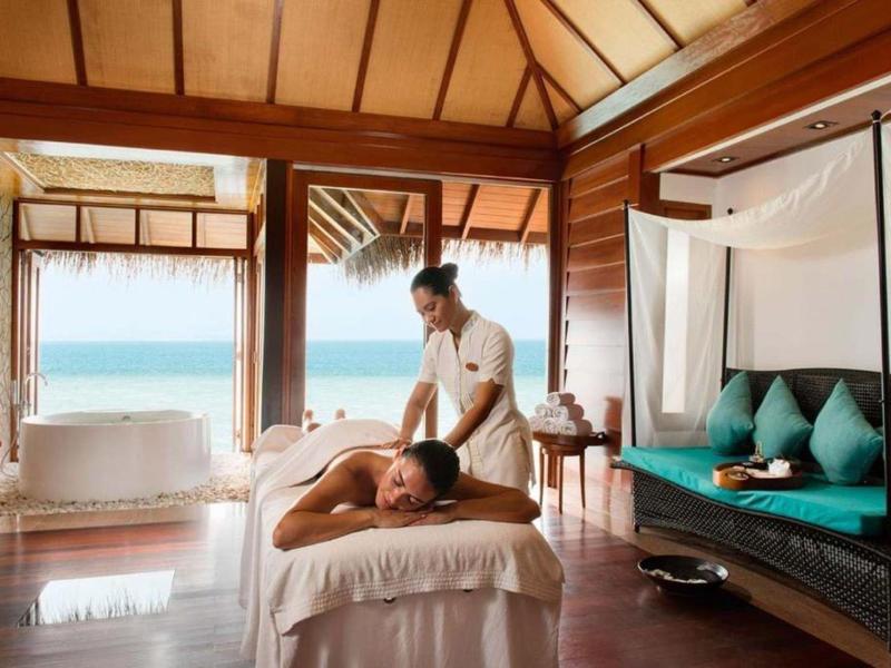 Massaggiatrice che tratta un cliente rilassato in una stanza benessere luminosa e tropicale con vista mare.