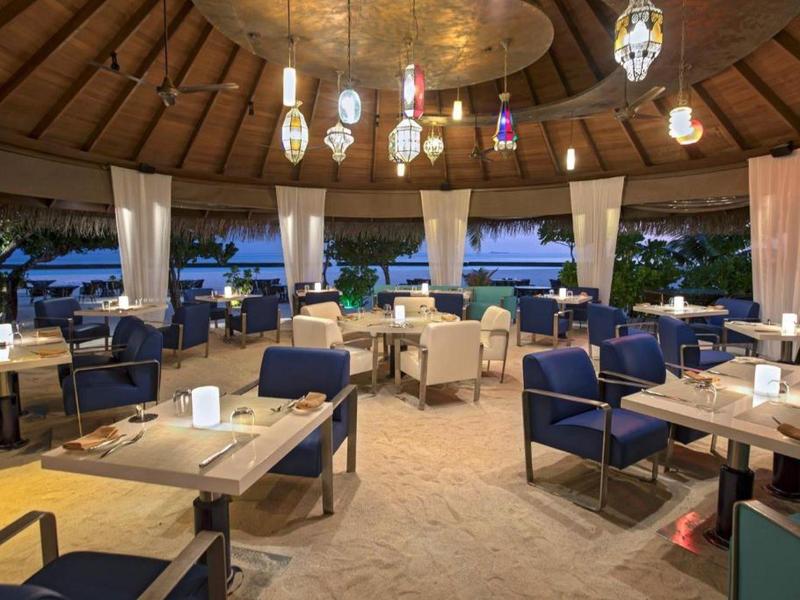 Area pranzo coperta aperta con mobili moderni e vista sul mare al crepuscolo.