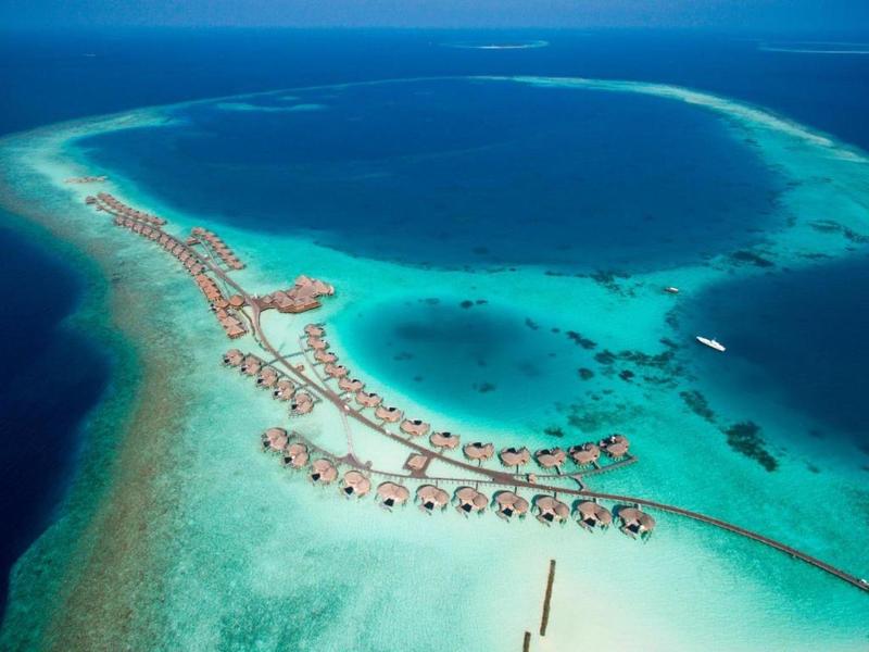Veduta aerea di un'isola tropicale con bungalow su palafitte e acqua turchese trasparente.