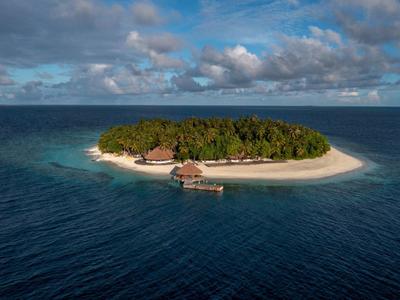 A small tropical island with lush greenery, white sandy beach, and wooden huts over clear blue water.