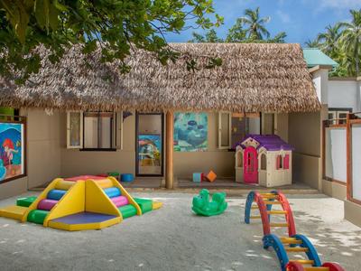 Outdoor kids' play area with colorful toys in front of a thatched-roof building.
