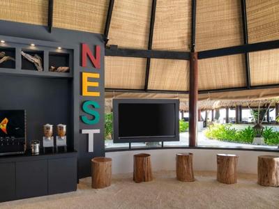 A cozy black TV area with colorful NEST letters and five wooden stools on a sandy floor.