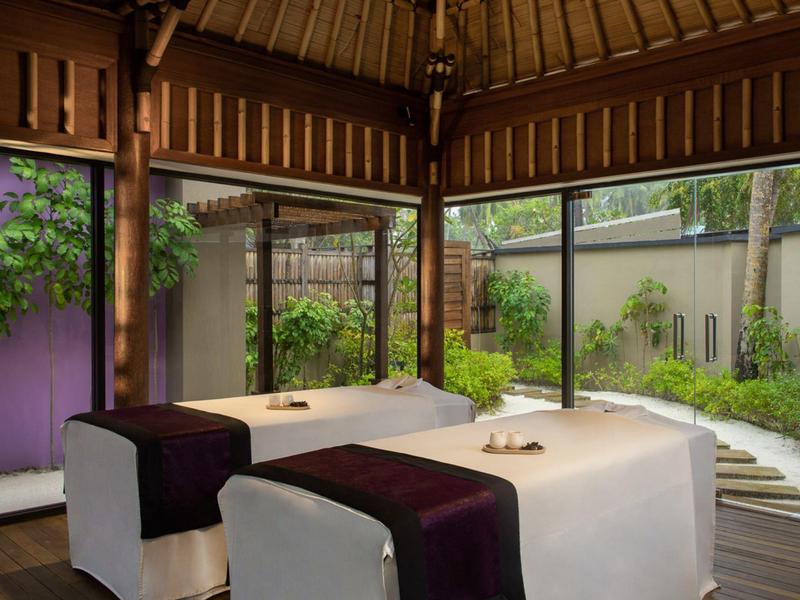 Cozy spa room with two massage beds, large windows, and a view of a peaceful garden.