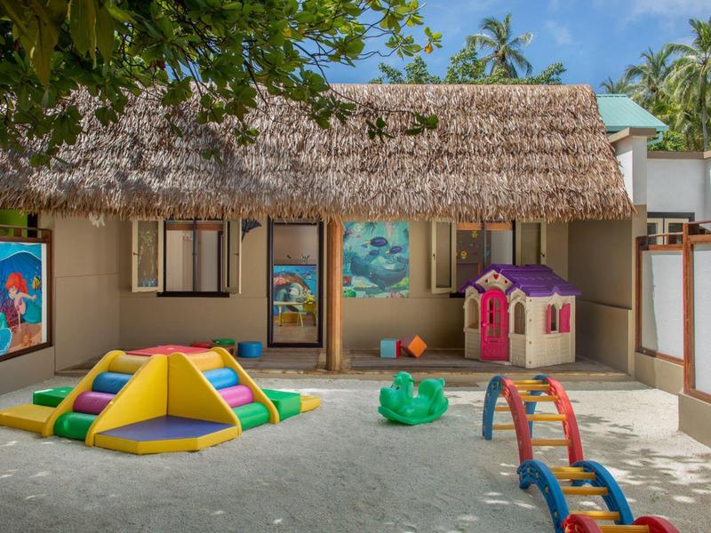 Outdoor kids' play area with colorful toys in front of a thatched-roof building.