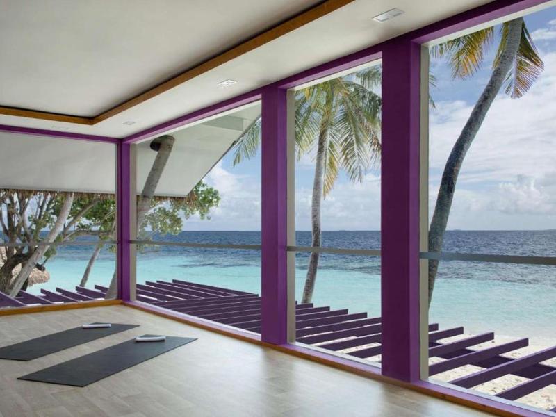 Open veranda with purple-trimmed pillars overlooking palm trees and turquoise ocean water.