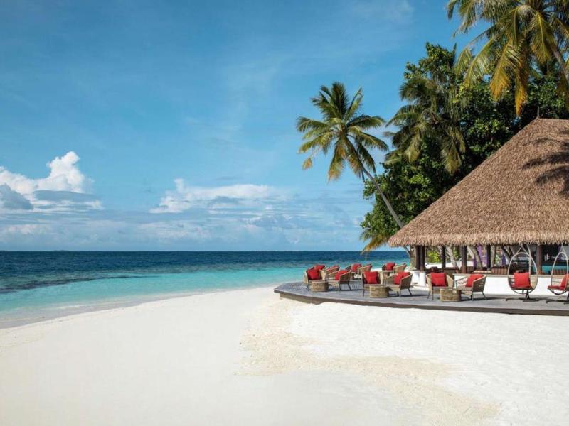 Beach resort with white sand, palm trees, clear blue sky, and ocean view.