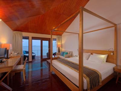 Pohodlný hotelový pokoj s postelí s nebesy a výhledem na moře přes velká okna.