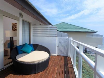 Dřevěná terasa s kulatým křeslem a výhledem na čisté moře pod částečně oblačnou oblohou.