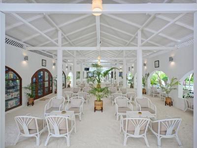 Sala da pranzo luminosa e bianca con tavoli bianchi, sedie e piante verdi.