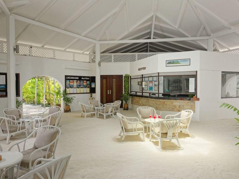 Světlý salonek s bílým ratanovým nábytkem a barem v otevřeném krytém prostoru.