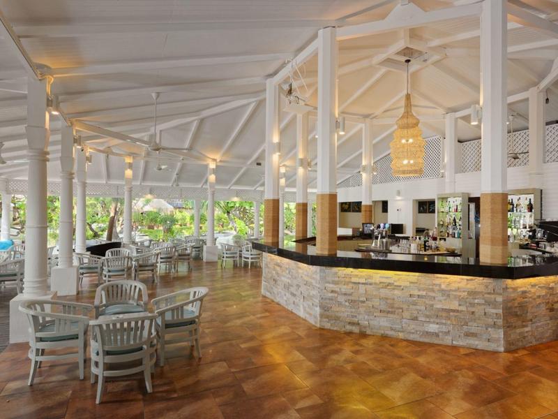 Světlá, otevřená restaurace s bílým nábytkem a moderním barem na dřevěné podlaze.