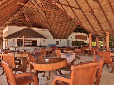 Otevřená jídelna s dřevěnými stoly a židlemi pod doškovou střechou.