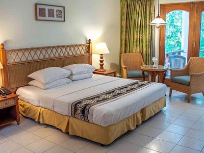 Pohodlný hotelový pokoj s velkou postelí, nočními stolky a posezením u velkých oken.