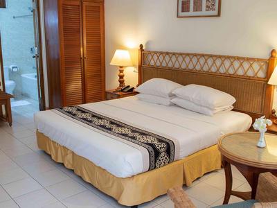 Hotelový pokoj s manželskou postelí, dvěma nočními stolky, židlí a přístupem do koupelny.