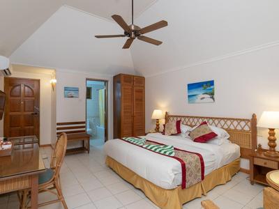 Prostorný hotelový pokoj s manželskou postelí, stropním ventilátorem a dřevěným psacím stolem.