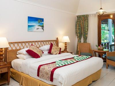 Pohodlný hotelový pokoj s velkou postelí, nočními stolky a výhledem do zahrady.