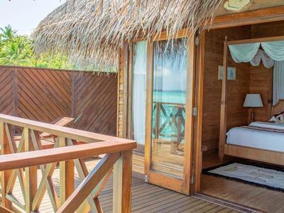 Dřevěná terasa s výhledem na moře, přístup do bungalovu se střechou z došek a otevřenou ložnicí.