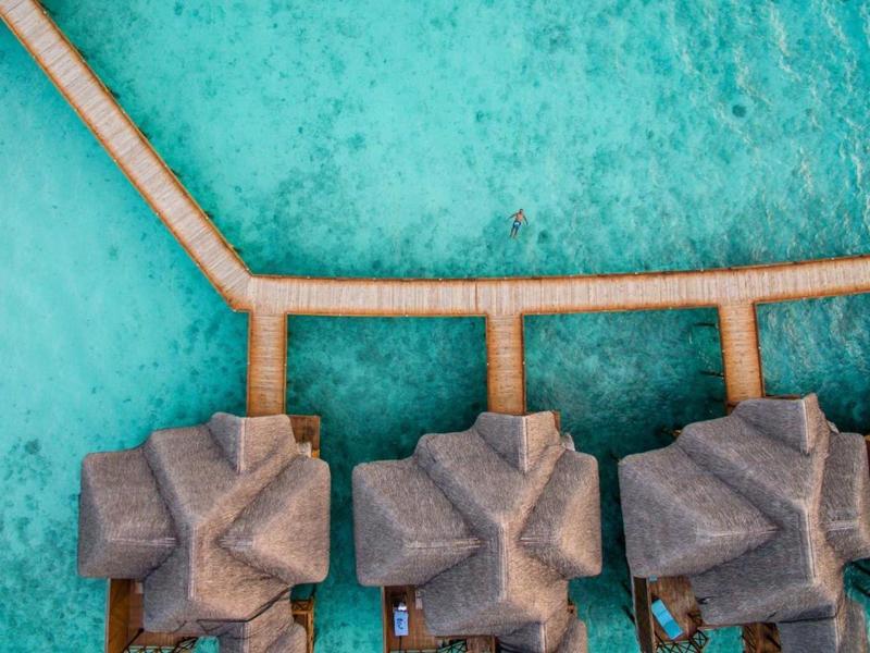 Tři plážové chatky spojené moly nad průzračnou tyrkysovou vodou.