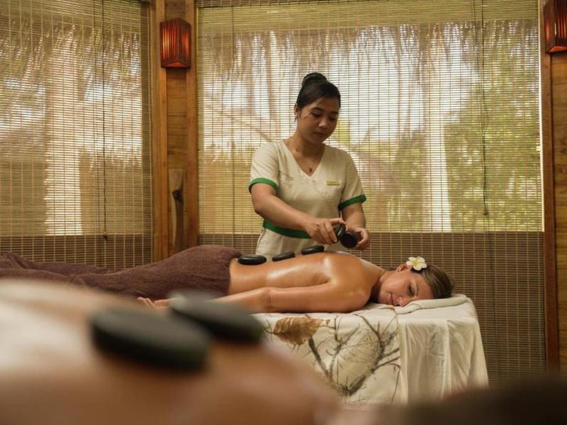 Žena dostává masáž horkými kameny v relaxačním wellness s bambusovými závěsy.