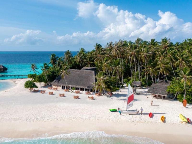 Tropická pláž s chatkou, palmami a čistou vodou pod modrou oblohou.