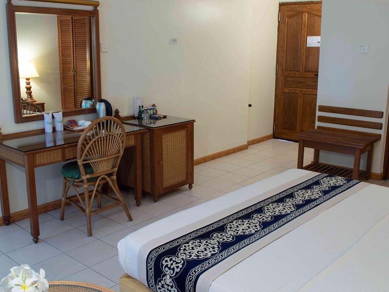 Jednoduchý hotelový pokoj se dvěma postelemi, psacím stolem, židlí a zrcadlem.