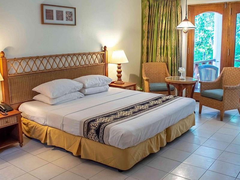 Pohodlný hotelový pokoj s velkou postelí, nočními stolky a posezením u velkých oken.