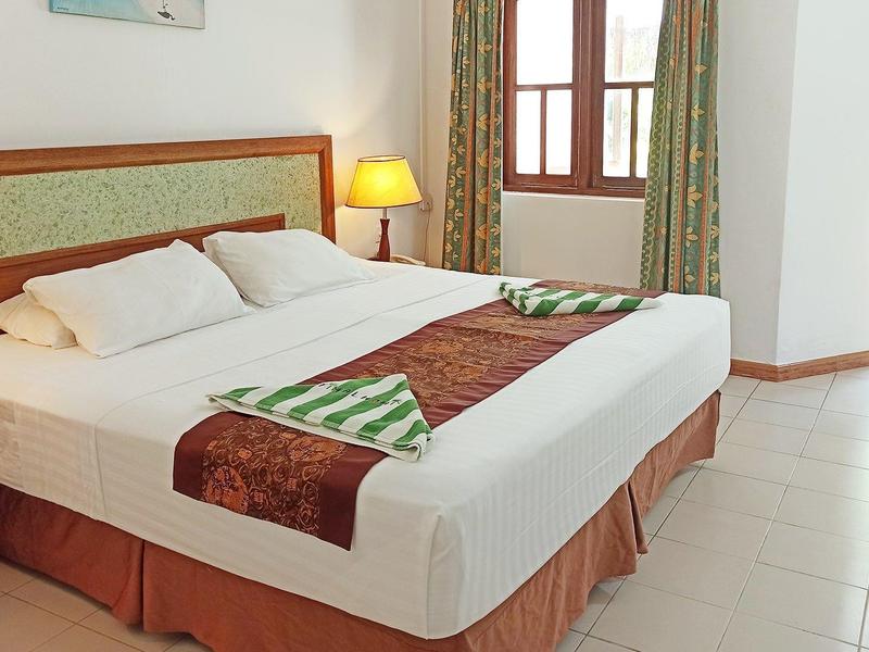 Světelný hotelový pokoj s velkou manželskou postelí, nočními stolky a přístupem na balkon.