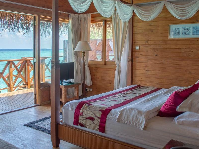 Dřevěný bungalov s manželskou postelí a výhledem na moře z terasy.