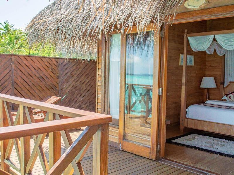 Dřevěná terasa s výhledem na moře, přístup do bungalovu se střechou z došek a otevřenou ložnicí.