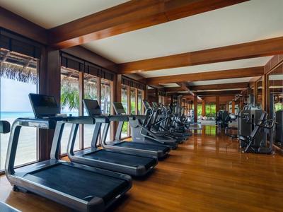 Palestra moderna con pavimenti in legno e tapis roulant davanti a grandi finestre con vista sul mare.