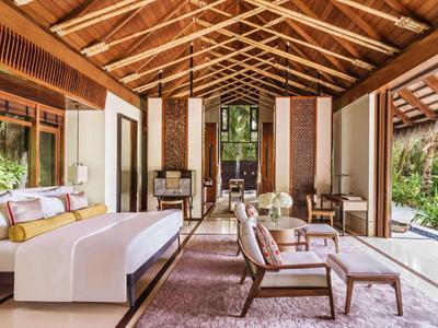 Spacious hotel suite with wooden ceiling, modern furniture, large bed, and glass walls.