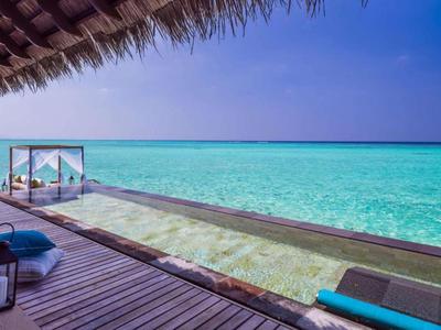 Infinity pool on a wooden deck overlooking a clear turquoise ocean under a blue sky.