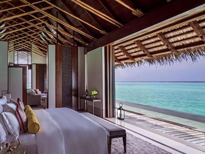 Luxurious beachfront villa with open wooden roof, spacious bed, and stunning ocean view.