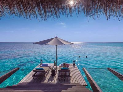 Wooden deck with lounge chairs and umbrella over clear blue tropical ocean.