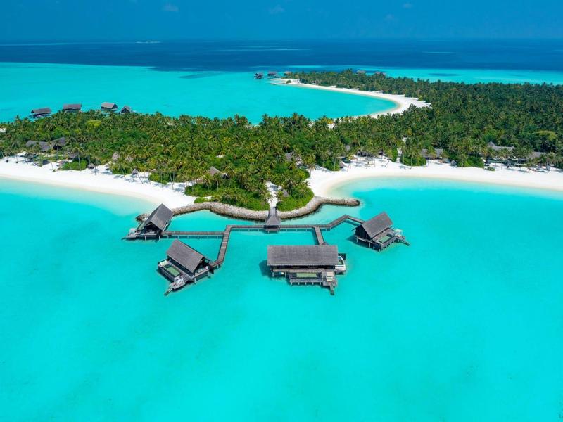 Overwater bungalows connected by wooden walkways over clear turquoise water at a tropical island resort.