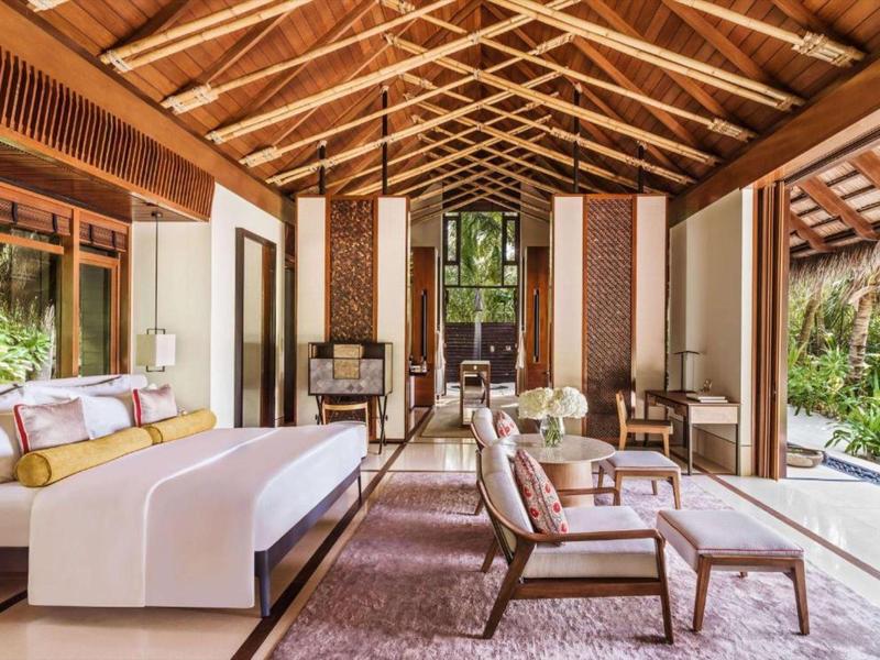 Spacious hotel suite with wooden ceiling, modern furniture, large bed, and glass walls.