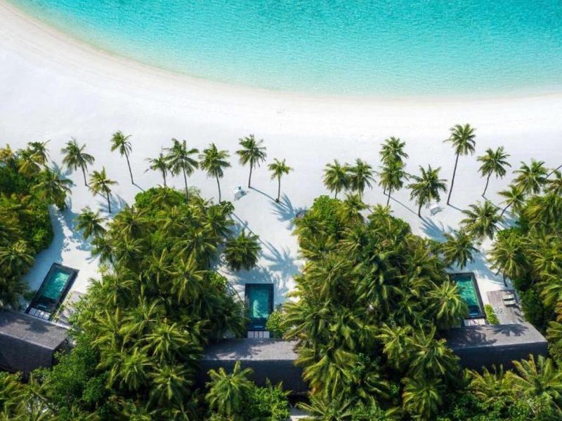 Aerial view of beachfront bungalows surrounded by palm trees and turquoise ocean water.