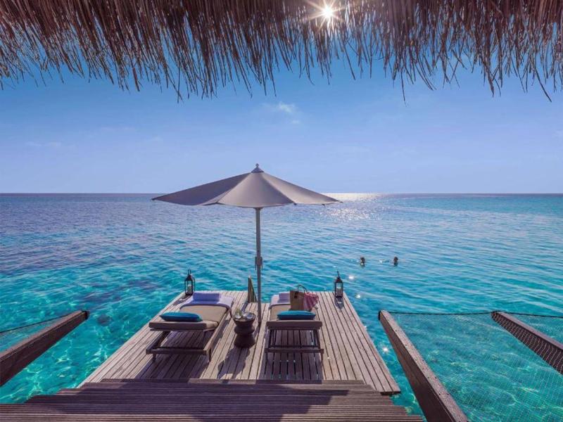 Wooden deck with lounge chairs and umbrella over clear blue tropical ocean.