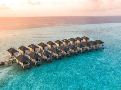 Überwasser-Bungalows in einer Lagune mit klarem, türkisfarbenem Wasser bei Sonnenuntergang.