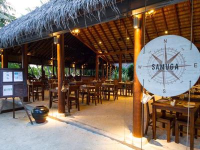 Offenes Restaurant mit Holzstühlen, Strohdach und rundem Kompass-Schild mit der Aufschrift "SAMUGA".