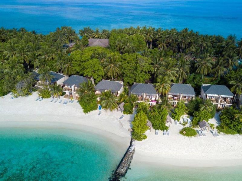 Tropische Insel mit weißen Sandstränden, grünen Palmen und kleinen Strandbungalows am türkisfarbenen Meer.