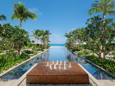 Piscine extérieure luxueuse avec fontaine et palmiers sous un ciel bleu clair