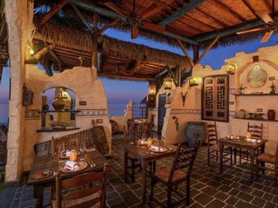 Restaurant en plein air avec toit en bois rustique et vue sur la mer au coucher du soleil.