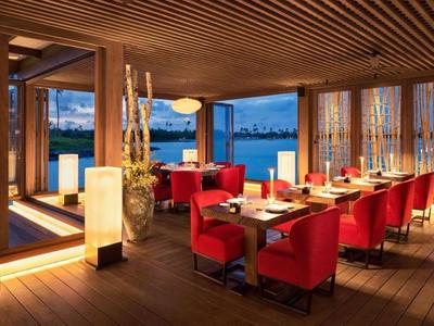 Restaurant moderne avec fauteuils rouges, plafond en bois et vue sur l'eau au crépuscule.
