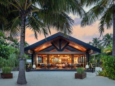 Otwarta restauracja na plaży z ciepłym oświetleniem i palmami o zachodzie słońca.