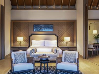 Nowoczesny pokój hotelowy z łóżkiem podwójnym, sofą, dwoma fotelami i drewnianą dekoracją.