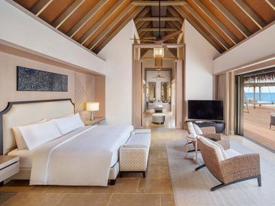 Przestronny pokój hotelowy z dużym łóżkiem, częścią wypoczynkową i widokiem na morze przez duże przesuwne drzwi.