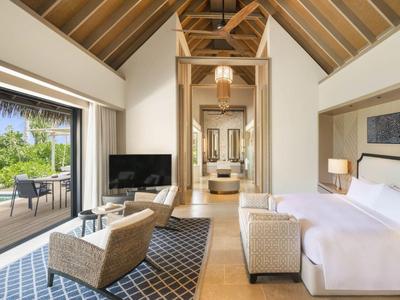 Jasny pokój hotelowy ze skośnym dachem, dużym łóżkiem, miejscem do siedzenia i widokiem na taras.