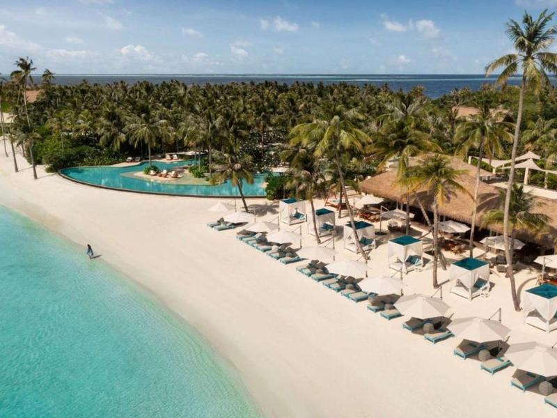 Biała piaszczysta plaża z leżakami, palmami i niebieskim morzem w słonecznym miejscu wypoczynkowym.